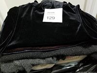 Stacked sweaters showing variety of colors and fabrics including black velvet and gray knit with sparkle.