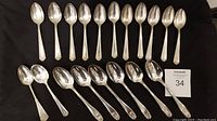 Complete set of 19 silver plated spoons arranged on black fabric, showing two different styles of spoons.