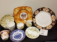 Overview of all plates, cups and saucers in the lot showing different patterns and colors, including Royal Albert cream and sugar, Bavaria cabinet plate, and Imari dinner plate.