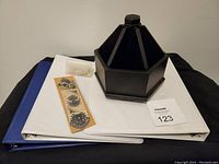 Two white binders with small boxes of brass fasteners and paper clips on top, and black turntable desk organizer.