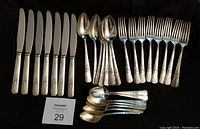 Full set of 29 pieces arranged including 7 dinner knives, 8 forks, 7 soup spoons, and 7 teaspoons on black background.
