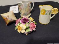 Four ceramic items arranged on black cloth: Royal Bayreuth jug, twinkle box, ceramic flower arrangement, Paragon creamer. Several pieces show crack lines.