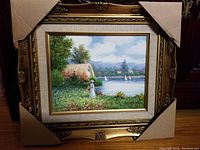 Framed signed landscape painting showing overall gold frame and image with protective cardboard corners.