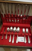 Full case showing assembled flatware set including knives, forks, spoons, butter knife in red felt-lined case.