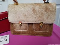 Front view of vintage handbag showing brown pony hair flap, front pocket compartments with gold tone clasps, and leather strap attachment.