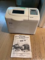 Closed view of Black & Decker breadmaker and the manual in front of it showing branding and size.