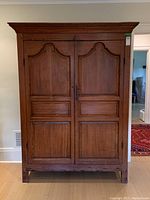 Front view of large antique wooden cabinet with carved paneled double doors and molding around the edges
