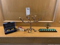 Full view of three Hanukkah candle holders displayed on a wooden surface including a silver-plated menorah, pair of brass candle holders in a blue case, and a brass menorah on a green base