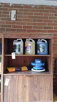 Wide shot of wooden shelving unit showing containers of windshield washer fluid, turtle wax buffer, and microfiber towels.