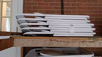Stack of five white folding chairs piled horizontally on top of each other showing folded structure and metal frames.