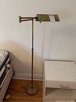 Full view of the metal floor lamp near a nightstand, showing height and base design.