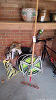 Garden rake standing in front of hose reel and bags of soil and potting medium, with bike frame visible (not included)