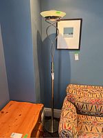 Full view of torchiere style floor lamp standing beside patterned armchair and wooden table, showing overall structure and design.