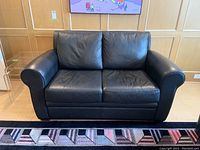 Front view of a black leather love seat with two cushions and rolled arms, showing the leather texture and condition.