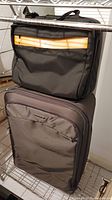 Photo showing the black Bree computer bag on top of the Briggs and Riley suitcase on metal shelving