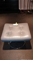 Top view of silver leather tufted ottoman seat with button accents on dark floor.