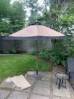 Fully assembled umbrella open on patio with metal base and protective cover laid beside it