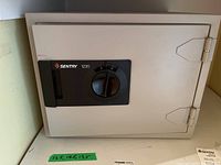 Closed Sentry 1230 safe on a shelf with note showing approximate measurements 16.5x14.5x13.5 inches.