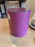 Front view of cylindrical resin side table with a round glass top showing glossy purple finish and slight surface marks.