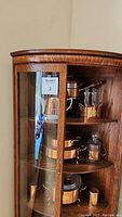 Side view of antique wooden corner china cabinet with glass doors partially open showing copper kitchenware inside