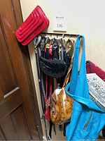 Photo showing hanging belts and handbags on hooks on a wall including red patent leather clutches, black textured handbag, turquoise tote, brown tooled leather handbag, and several belts of varying colors and styles.