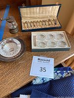 Set of 12 colorful enameled handle caviar spoons in a lined box, 6 crystal caviar bowls in box, silver-plated glass caviar bowl, and vintage pepper mill on table.