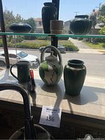 Photo of nine assorted ceramic items on windowsill, including vases, pitcher, bowls, and bird figurine.