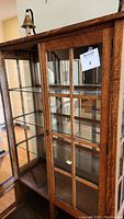 Front view of wooden china cabinet showing glass paneled door with grid design and interior glass shelves.