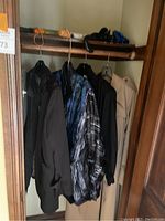 Overall view of coats hanging in closet including a black coat, a brightly patterned coat, and a tan coat.