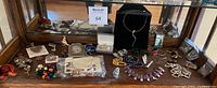Photo of various costume jewelry pieces including necklaces, pins, earrings, bracelets displayed on wooden shelf.