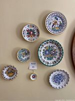 Overview photo of all seven decorative plates arranged on a wall showing varying sizes and colorful hand-painted floral and bird designs