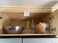 Wide shot of a shelf showing silver bowls, glass decanter, decorative jar, and Vincent bottle