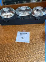 Three clear Orrefors glass votive candle holders displayed on a black box on wooden surface with Maxsold auction number shown.
