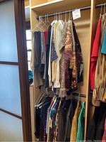 Closet rod with various women’s clothing, multiple sweaters, blouses, and pants hung neatly