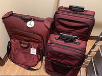 Four Briggs and Riley luggage pieces in burgundy: large bag, medium bag, garment bag, and laptop case all arranged upright.