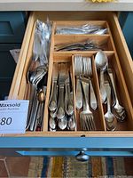 Full drawer of silverware showing multiple knives, forks, spoons, and teaspoons laid out visibly in compartments of a wooden organizer.
