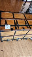 Photo showing the top and sides of wooden dresser trunk with black metal reinforcements on the edges and corners, placed on wooden floor.