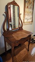 Full view of vintage wooden vanity with attached mirror and curved carved supports on sides.