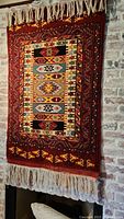 Full view of red native design wall rug hanging on brick wall showing overall pattern and fringe tassels at top and bottom.