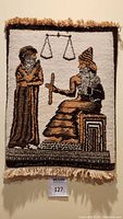Front view of wool tapestry showing two figures and legal scale symbol. Included hanging tag with lot number 127.