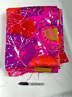 Folded fabric showing vibrant pink, red, purple, olive green, and white leaf patterns with a Sharpie pen for scale.