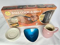 Photo showing boxed Nordicware bake, cook & serve baking tray set, pink Le Creuset jug, silver-plated Reed & Barton triangular dish, and four white saucers