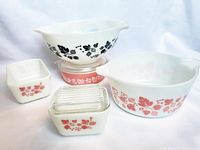 Five Pyrex pieces arranged showing both pink and black gooseberry patterns including two fridgies with glass lids, a casserole with lid, and two bowls.