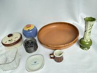 Overview of vintage houseware items including brown lidded dish, blue Lindt Stymeist sugar dish, wooden bowl, green vase, brown Hall creamer, stack of metal-edge coasters, and a small white plate