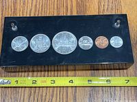 Top view showing all six coins embedded in black Lucite block with measuring tape for scale.