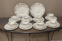 Full view of 8 tea trios and 2 serving plates arranged on a table showing floral pattern and gold trim