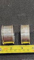 Two silver napkin rings placed side-by-side with measuring tape showing approximate size of each ring around 1.5 to 2 inches in diameter, showing the full profile of the rings.