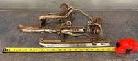 Full view of antique wooden and steel skating blades with leather straps and measuring tape indicating size approximately 15 inches.
