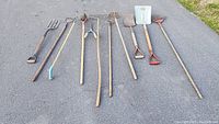 Full collection of 9 garden tools laid out side by side on pavement, showing various types of tools with wooden handles and metal heads.