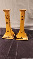 Front view of pair of Limoges candlesticks with swallow motifs on ochre-yellow base.
